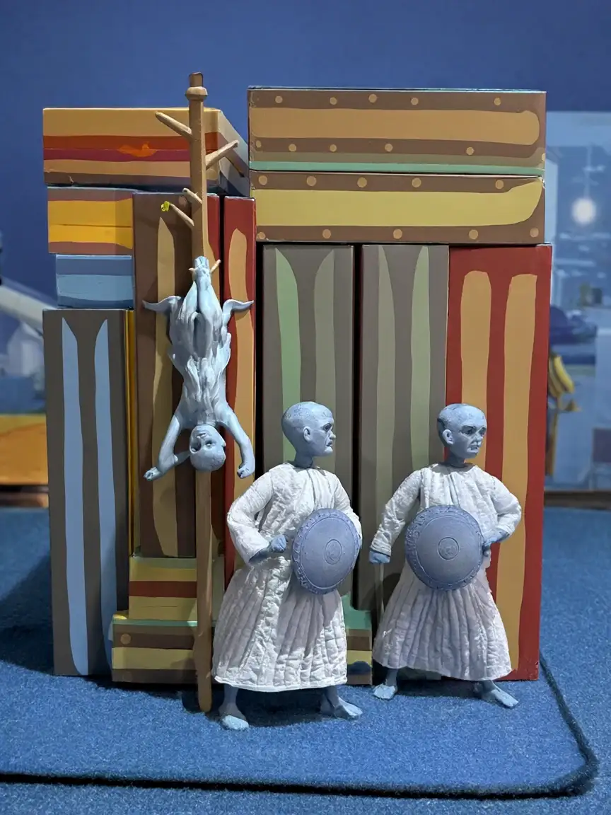 Box art: pale figures with round shields stand before a painted cardboard palace, one hanging upside down from a pole.